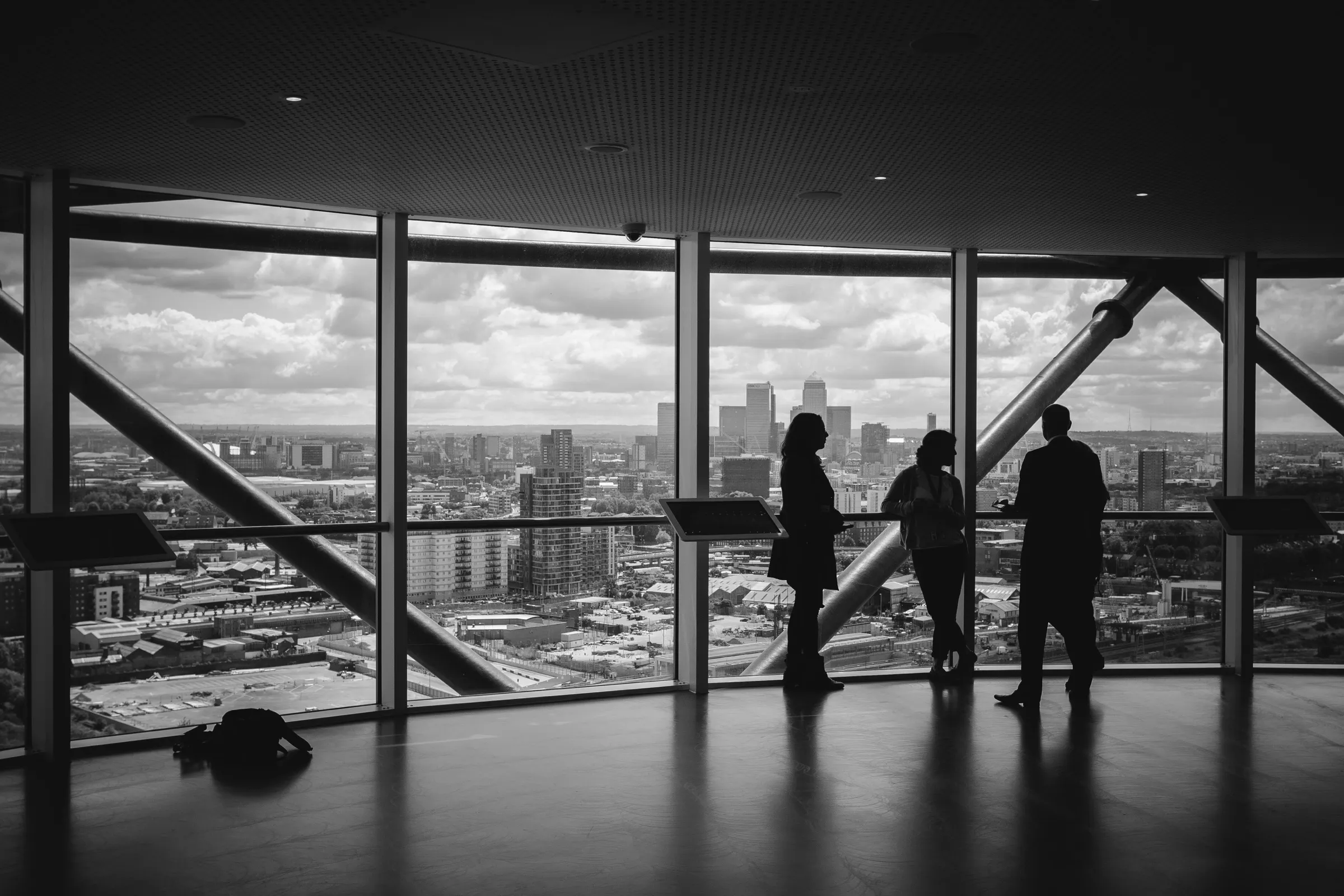 Three people silhouetted against tall windows high above a city