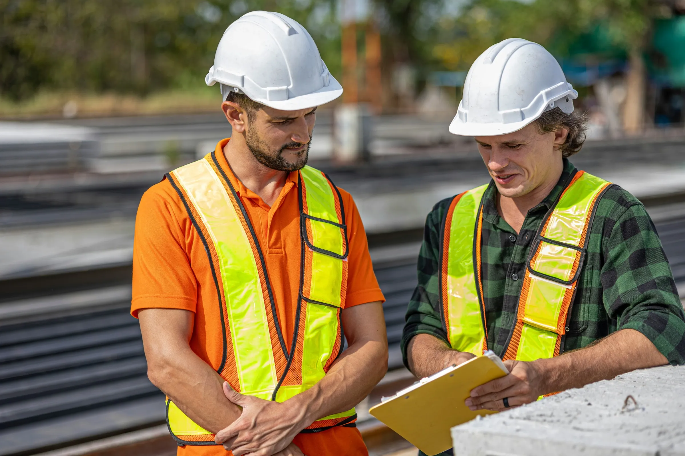 Two safety practitioners in hard hats reviewing a document on a building site
