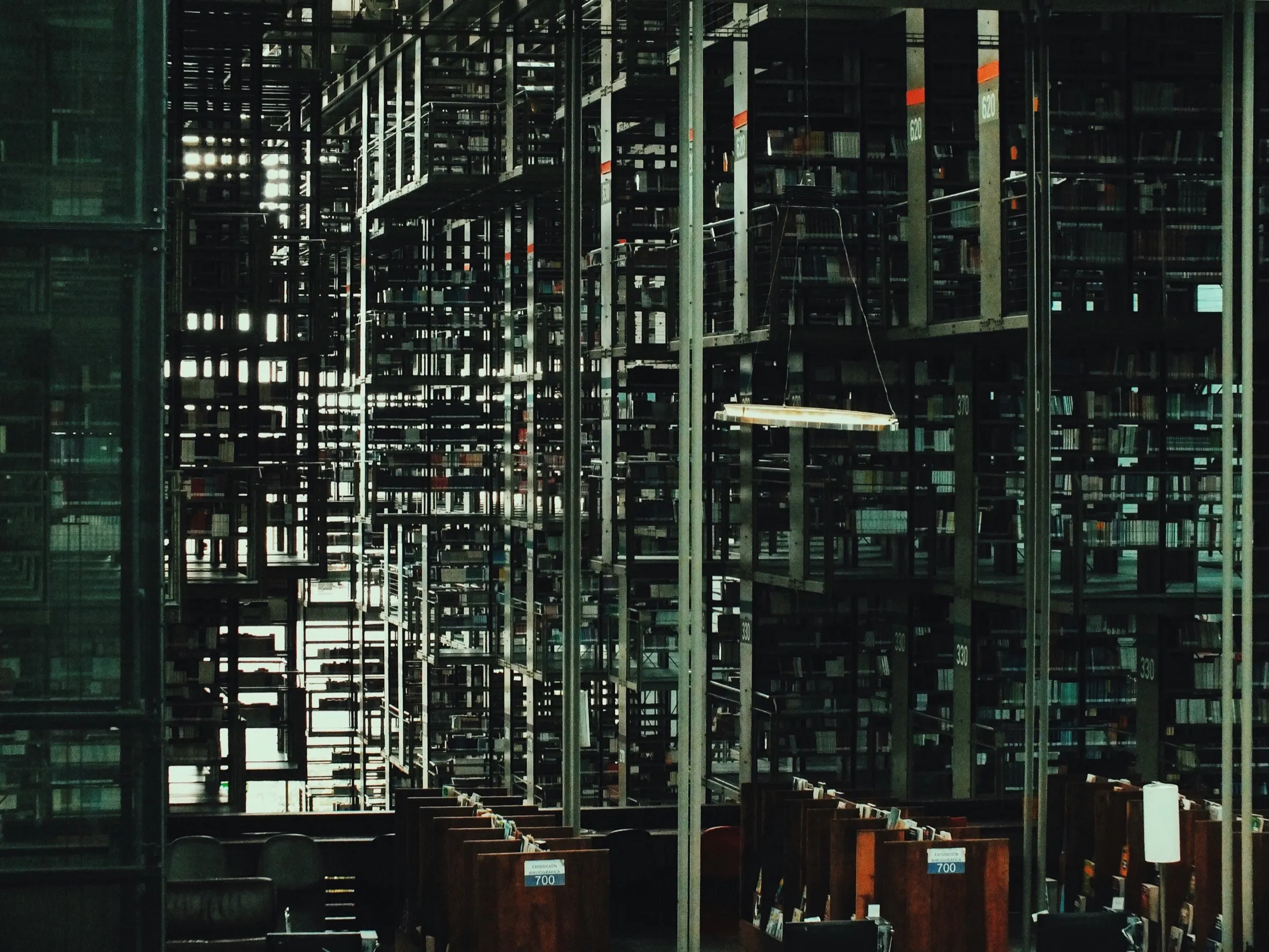 Tall steel stacks of books rising through a dim library hall